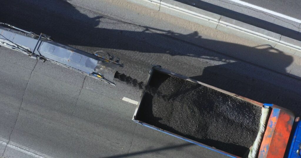 A machine performing asphalt milling services, grinding old asphalt and loading it into a truck for removal.