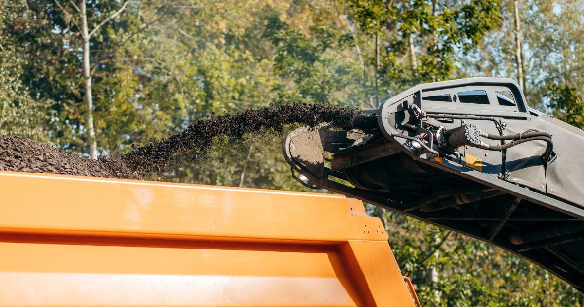 A machine performing asphalt milling services, grinding old asphalt and loading it into a truck for removal.