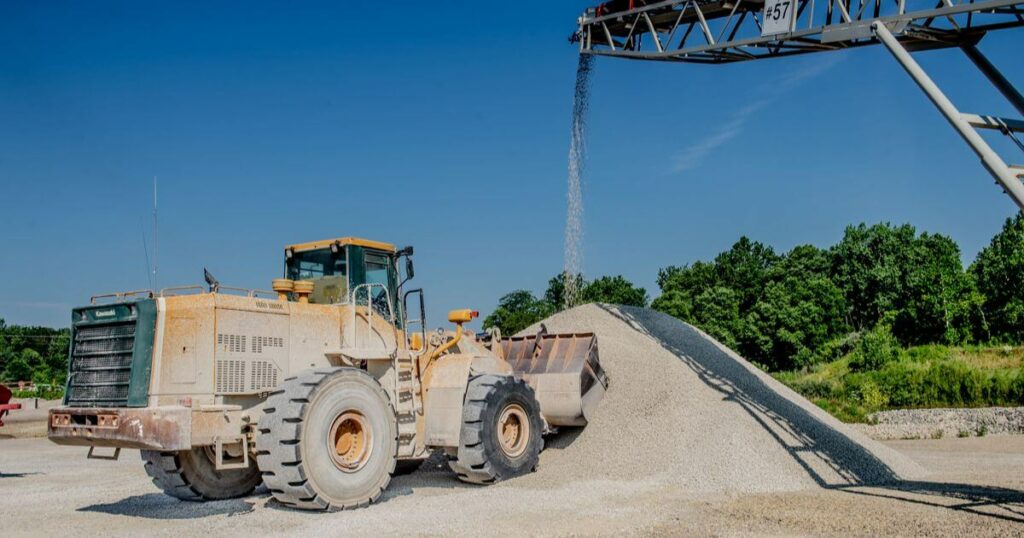 A construction vehicle next to a conveyor system pouring crushed stone material, showing the efficiency and capability of mobile crushing services.