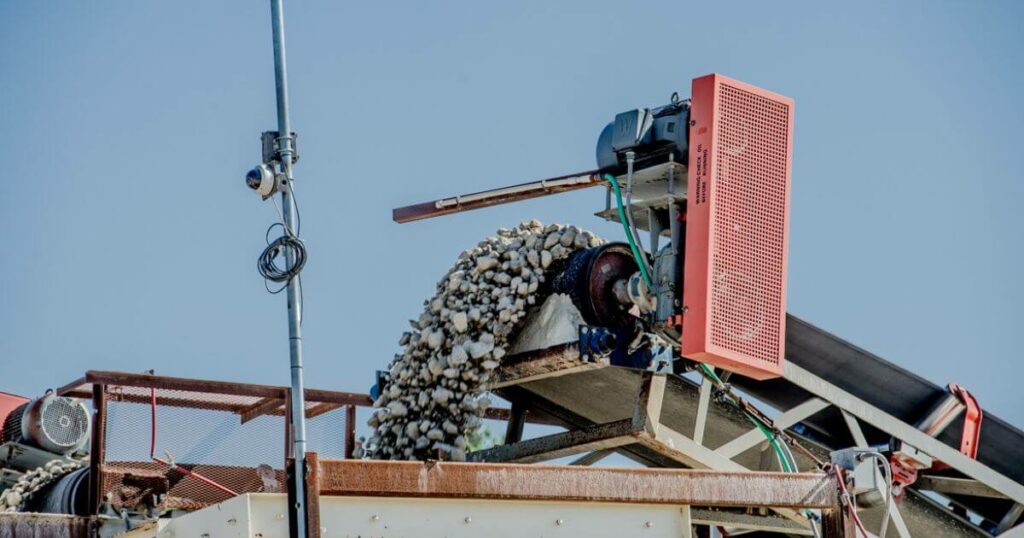 A close-up of a mobile crushing machine in operation, with large rocks being processed on a conveyor system, highlighting the technology used in mobile crushing services.